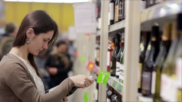 Mujer selecciona el vino en los estantes de la tienda — Vídeos de Stock