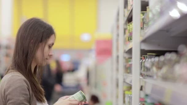 Mujer joven elige comida enlatada en la tienda — Vídeos de Stock