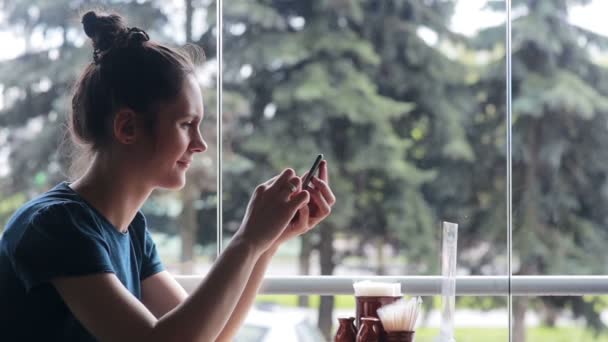 Женщина с помощью смартфона сидит у окна — стоковое видео