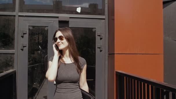 Mulher de negócios sexy usando smartphone andando perto de construção edifício de negócios, steadicam tiro. lento mo — Vídeo de Stock