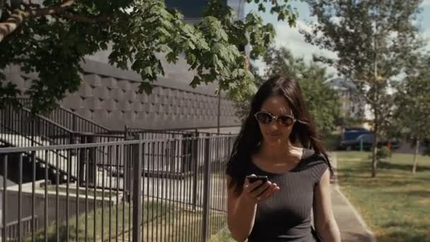 Femme d'affaires sexy en utilisant smartphone marchant près du bâtiment d'affaires, steadicam shot. ralenti — Video