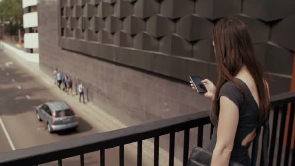 Sexy donna d'affari utilizzando smartphone in piedi su un ponte con vista sulla strada, colpo steadicam. lenta mo — Video Stock