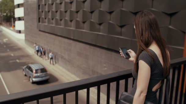 Sexy Geschäftsfrau mit Smartphone auf einer Brücke mit Blick auf die Straße stehen, Steadicam-Aufnahme. Langsames Wachstum — Stockvideo