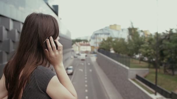 Sexy Geschäftsfrau mit Smartphone auf einer Brücke mit Blick auf die Straße stehen, Steadicam-Aufnahme. Langsames Wachstum — Stockvideo