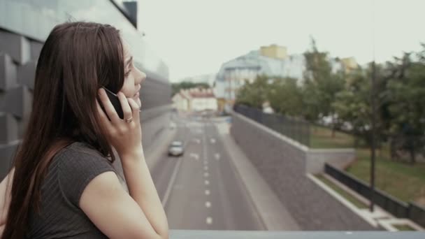 Sexy mujer de negocios utilizando el teléfono inteligente de pie en un puente con vistas a la carretera, steadicam disparo. lento mo — Vídeo de stock
