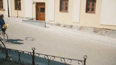 Young woman walking in old town looking around with a retro bike with flowers in a basket in summertime, slow mo