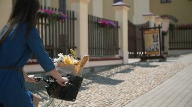 Kız bir sepet içinde paperbag içinde çiçek ve Fransız ekmeği ile şehirde bir bisiklet sürme, yavaş mo, steadicam atış