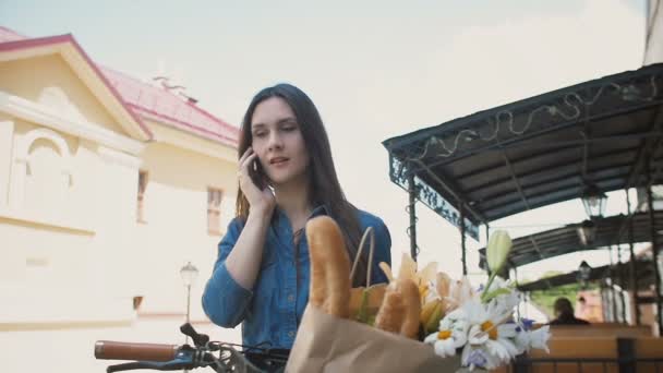 Belle fille debout dans la rue avec un vélo parlant au téléphone et souriant, lent mo — Video