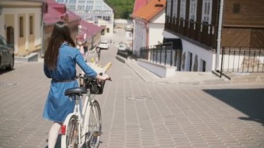 Bir sepet içinde çiçeklerle sokakta bisikletini yürüyen güneş gözlüğü takan kız, yavaş mo, steadicam atış