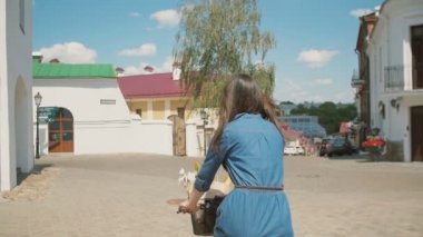 Sokakta bir sepet içinde çiçeklerle bisiklete binen mavi elbiseli bir kızın geri görünümü, yavaş mo, steadicam atış