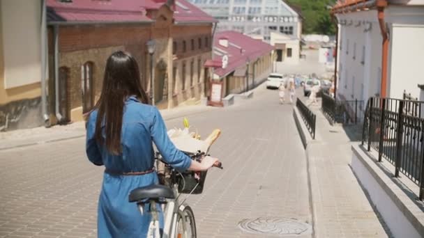 Tyttö yllään aurinkolasit kävely hänen pyörä kadulla kukkia korissa, hidas mo, steadicam ammuttu — kuvapankkivideo