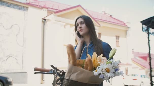 Menina bonita de pé na rua com uma bicicleta com cesta falando no telefone e sorrindo, slow mo — Vídeo de Stock