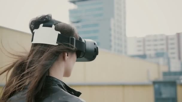 Брюнетка с размахивающимися волосами использует гарнитуру 3D Virtual Reality на крыше. 4k — стоковое видео