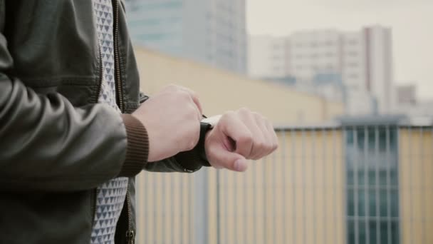 Homem usando seu smartwatch touchscreen em pé no telhado, em seguida, se afasta. mãos fechadas. 4k — Vídeo de Stock