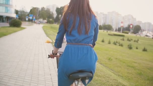 一个女孩骑着一辆自行车用鲜花和法式面包在篮子里市、 慢动作模式、 斯坦尼康来拍摄镜头后面观 — 图库视频影像