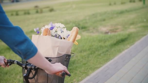 Κορίτσι τα χέρια στο τιμόνι ενός ποδηλάτου, λουλούδια και ψωμί σε ένα καλάθι, Ποδηλασία στην πόλη, Μενεγάκη, steadicam βολή — Αρχείο Βίντεο