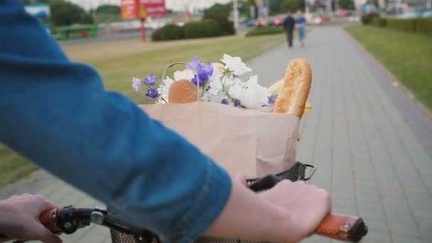 Mulher mãos no guidão de bicicleta com flores e pão na cesta como ela anda na rua, câmera lenta, steadicam tiro — Vídeo de Stock