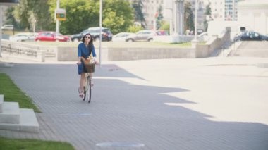 Tahrik arabalar, yavaş mo ile meşgul road yakınındaki bir bisiklet sürme güzel bir esmer kız arkadan görünüm