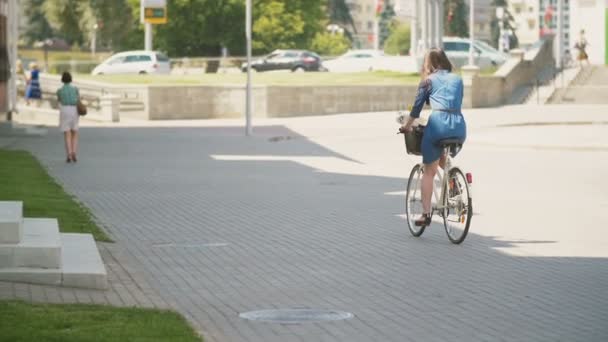 Rückansicht eines schönen brünetten Mädchens auf einem Fahrrad in der Nähe von viel befahrenen Straße mit angetriebenen Autos, langsam mo — Stockvideo