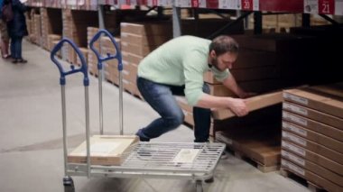 Bir adam raftan bir kutu alıyor, tramvaya koyuyor, depodaki listesini kontrol ediyor.