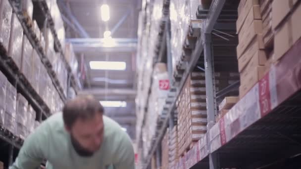En man sätter lådor tillbaka på hyllorna i ett lager och går bort från kameran — Stockvideo