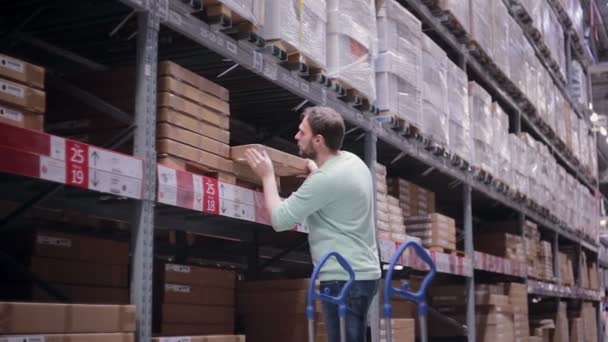 En man tar en låda från en hylla, sätta den på vagnen i ett lager — Stockvideo