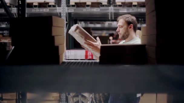 A man is looking for necessary package, taking one from the shelf with cardboard boxes in a storage warehouse — Stock Video