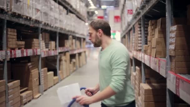 Een man draait een trolley achteruit in een magazijn — Stockvideo