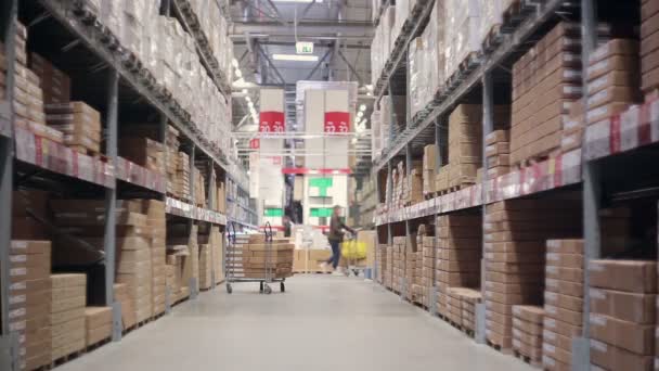 A funny man is surprised by a variety of goods walking between shelves of goods in a warehouse — Stock Video