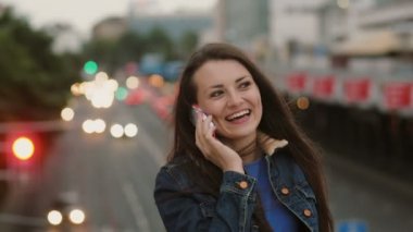 mutlu, gülümseyen güzel kadın telefonda konuşurken köprüde duruyor ve rüzgar saçlarını üflüyor. 4k