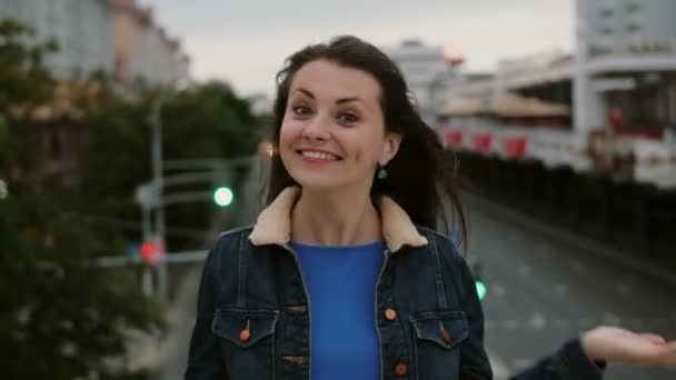 Веселую, счастливую, улыбающуюся девушку, стоящую на мосту, веселую, позирующую, посылающую поцелуи, смотрит в камеру. 4K — стоковое видео