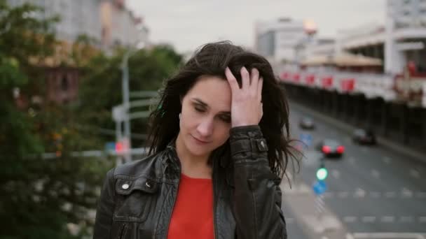 Sonriente hermosa chica de pie en el puente, tocándose el pelo y mira a la cámara. El viento sopla su pelo largo. 4K — Vídeos de Stock