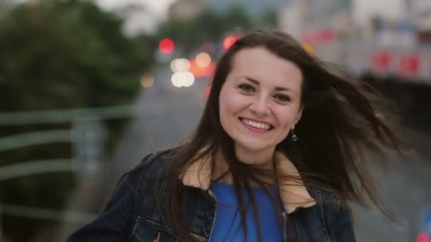 El viento sopla pelo largo hermosas mujeres jóvenes. chica sonriente de pie en el puente por la noche y mira a la cámara. 4K — Vídeo de stock