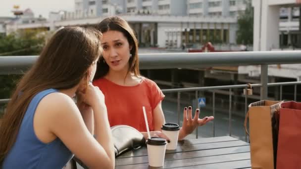 Wanita cantik minum kopi berkomunikasi di sebuah kafe dengan pemandangan lalu lintas, berbicara setelah belanja. 4k — Stok Video