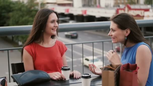 Hermosas mujeres tomando café se comunican en un café con una vista del tráfico, hablando después de ir de compras. 4k — Vídeos de Stock