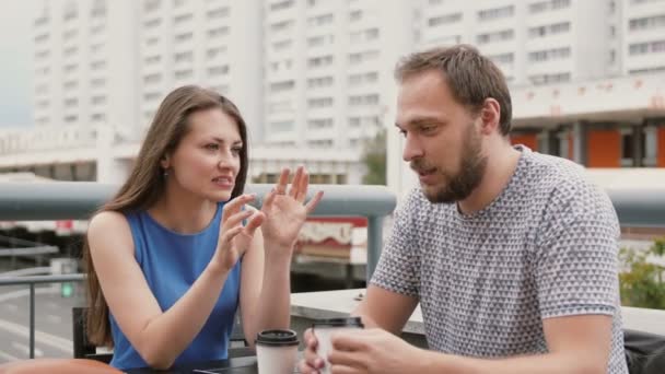 Een aantrekkelijk jong stel in een café op straat, een vrouw zegt emotioneel iets aan de man. 4k — Stockvideo