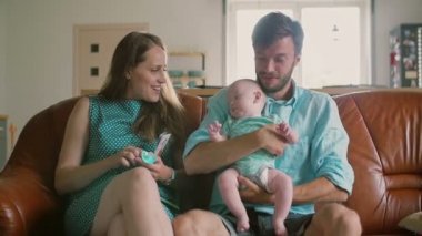Dört kişilik aile kanepede oturuyor: baba yeni doğan oğlunu tutuyor ve kızı yanlarına neşeyle atlıyor. Yavaş mo