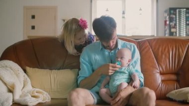 Young fatheris sitting on the sofa caressing his newborn son while his daughter is smiling in the back. Slow mo
