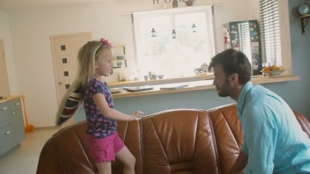 Ein junger Vater und seine süße fröhliche kleine Tochter bei einer Kissenschlacht auf dem Sofa. Zeitlupe, Steadicam-Aufnahme — Stockvideo