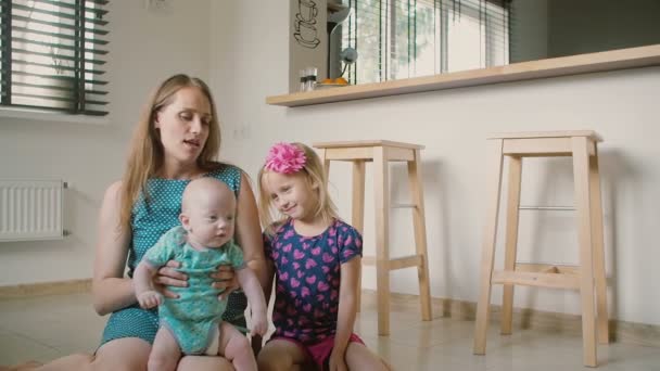 Mooie jonge moeder zit op de keuken vloer met haar baby zoon en schattige kleine dochter. Slow Motion — Stockvideo