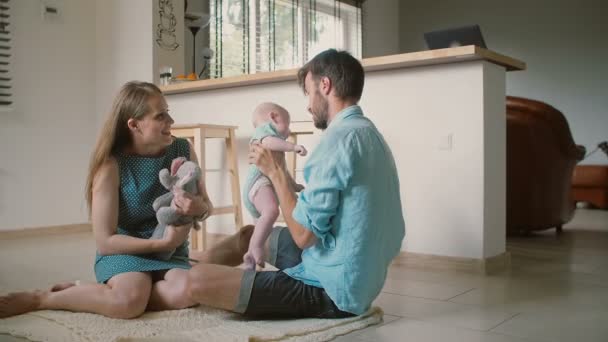 Young father holds up his baby son and gives him a gentle kiss while his beautiful wife is sitting next to him. Slow mo — ストック動画