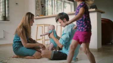 Mutlu anne-babalar mutfak katta oturuyor ve kızları etrafında koşuşturuyor ise bebeklerini tutuyorlar. Yavaş mo