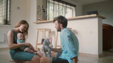 Young mother is playing with her baby son sitting on her lap with her husband sitting next to her and talking. Slow mo