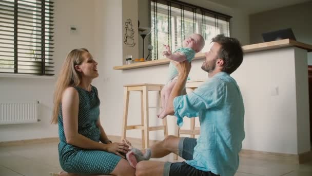 Een mooie moeder geeft haar baby zoon aan de vader die hem hoog opheft en de baby vrolijk glimlacht. Slow mo — Stockvideo