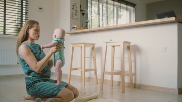 Uma bela jovem mãe está segurando seu adorável bebê sorridente ajudando-o a se levantar e falar com ele. Movimento lento — Vídeo de Stock