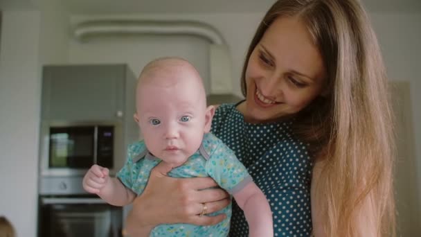 彼女はカメラに直面して彼女の愛らしい赤ちゃんを保持している間、若い母親の顔のクローズアップ。スローモーション、ステディカムショット — ストック動画