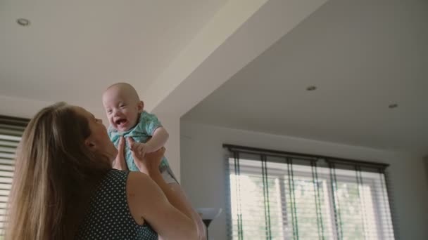 Una cara feliz de risa de un precioso bebé cuya madre lo sostiene en el aire y le sonríe. Lento mo — Vídeo de stock