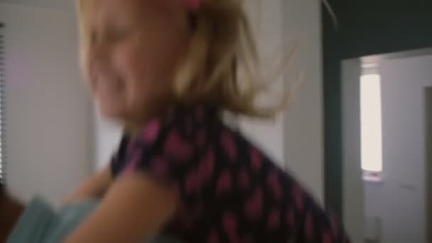 Young father is jumping around the house with his cute little daughter on his back. Slow mo, Steadicam shot — Stock video