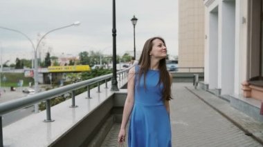 Alışveriş çantaları ile şehirde yürüyen mavi elbiseli güzel genç kadın, etrafına bakar, yavaş mo stedicam vurdu