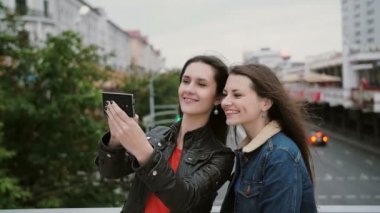 İki kız en iyi arkadaş selfie çekiyor, şehir köprüsünde duruyor, konuşuyor, gülümsüyor, gülüyor. yavaş mo.
